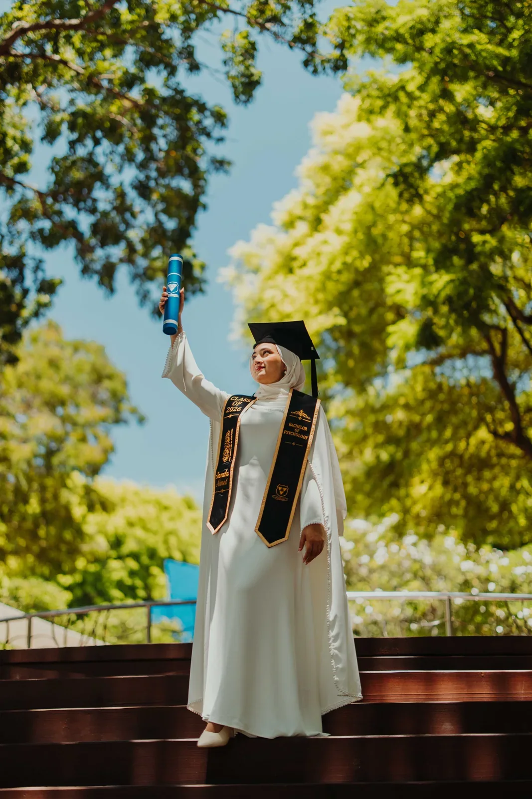 A graduate celebrating with her certificate beneath green trees